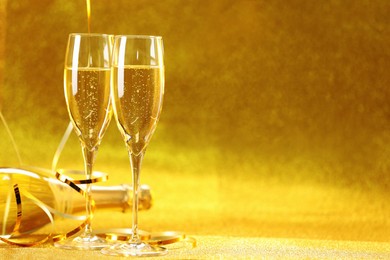 Photo of Champagne in glasses and bottle on golden background. Space for text