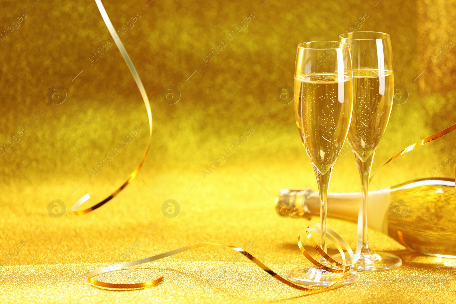 Photo of Champagne in glasses and bottle on golden background. Space for text