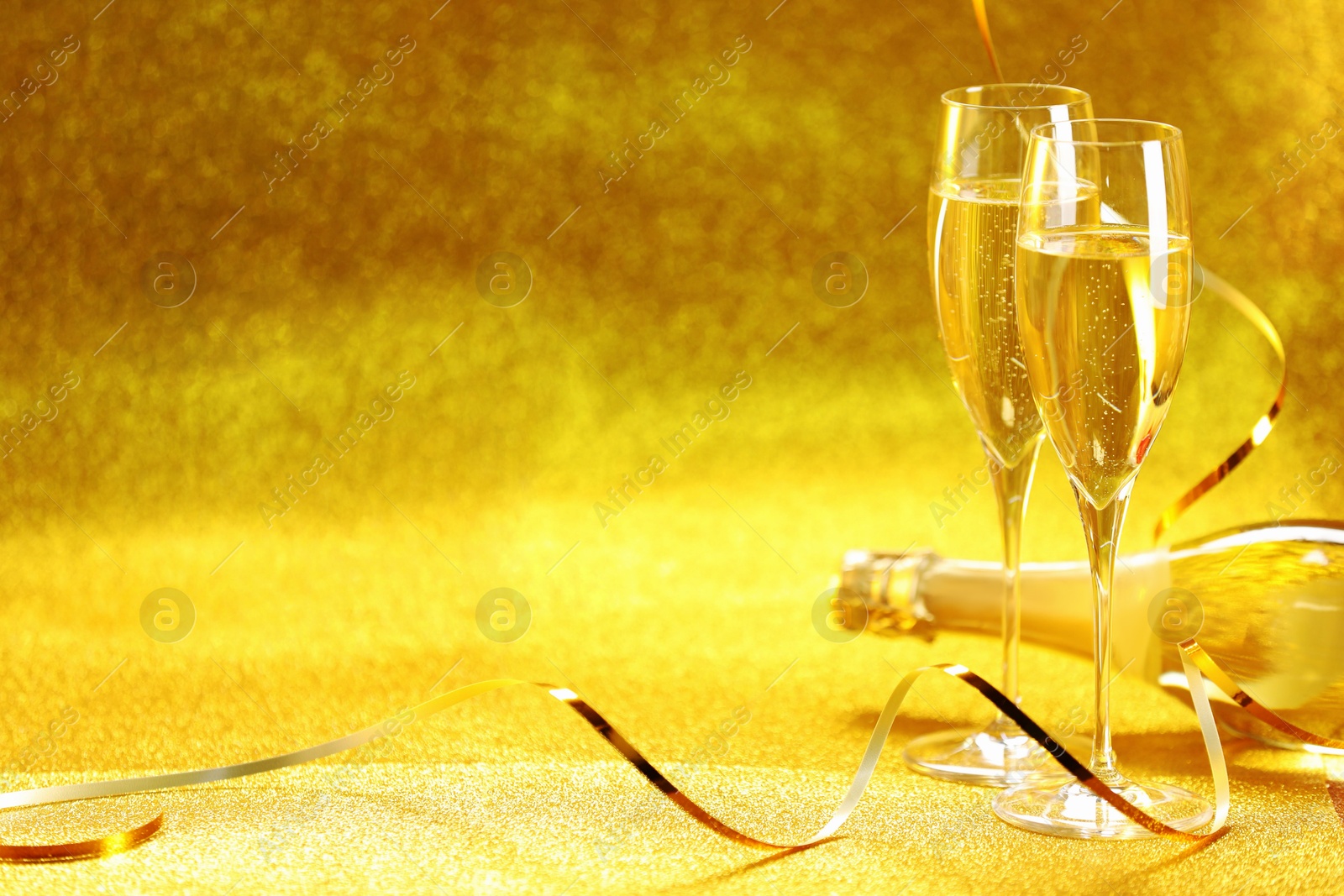 Photo of Champagne in glasses and bottle on golden background. Space for text