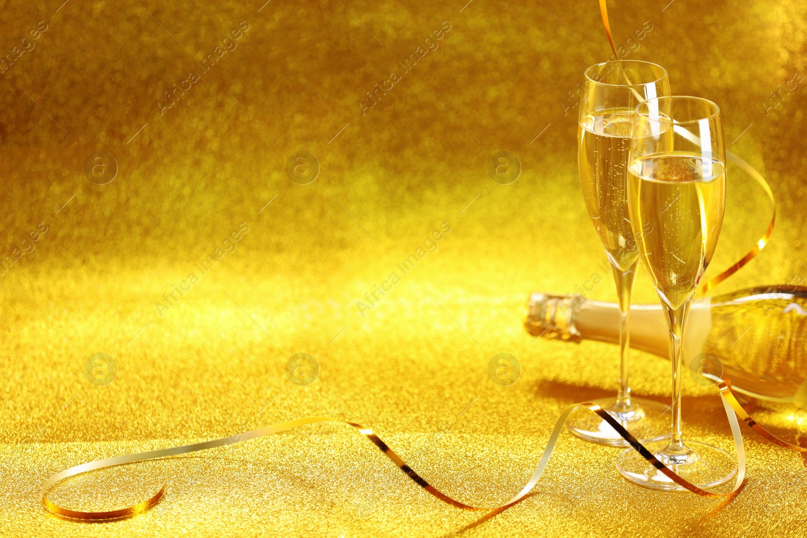 Photo of Champagne in glasses and bottle on golden background. Space for text