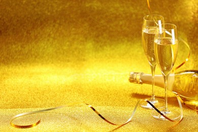 Photo of Champagne in glasses and bottle on golden background. Space for text