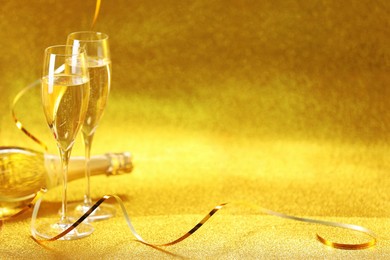 Photo of Champagne in glasses and bottle on golden background. Space for text