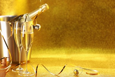 Photo of Champagne in glasses and ice bucket with bottle on golden background. Space for text