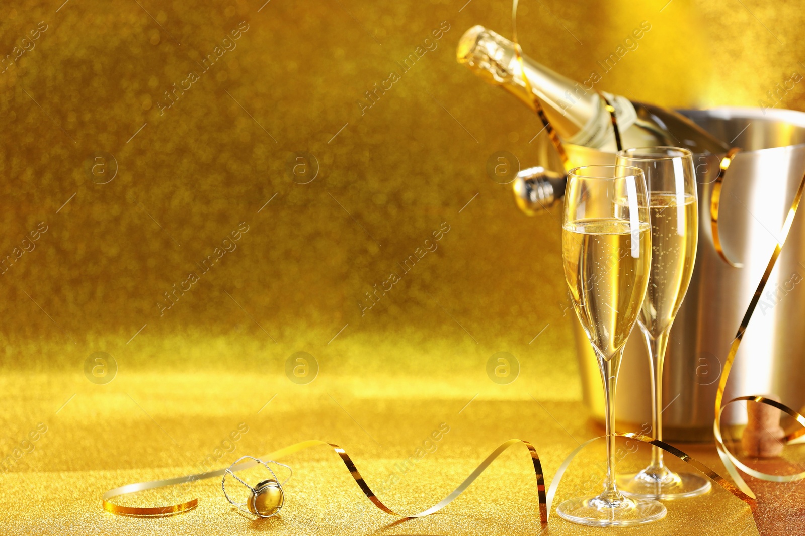 Photo of Champagne in glasses and ice bucket with bottle on golden background. Space for text