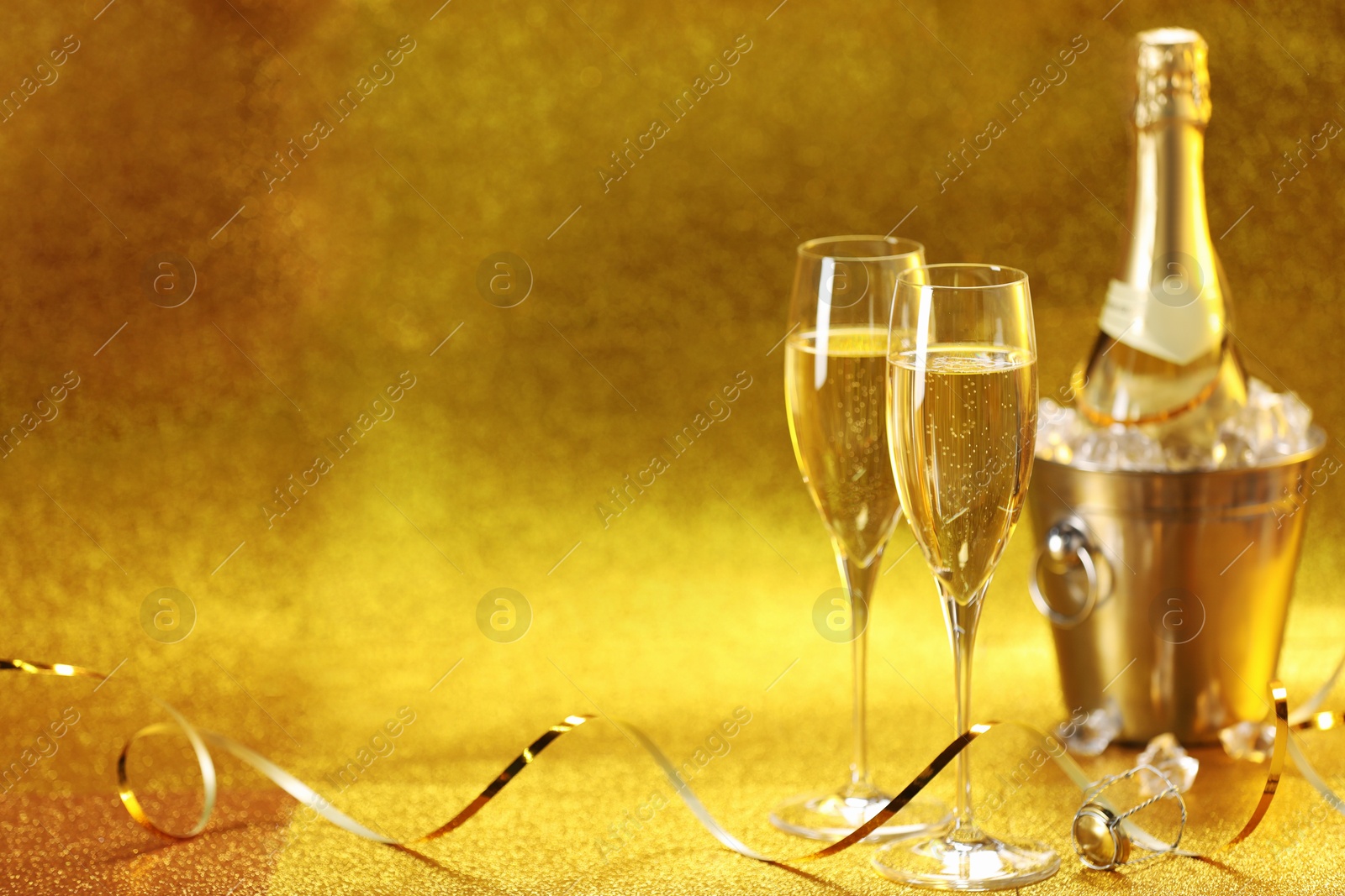 Photo of Champagne in glasses and ice bucket with bottle on golden background. Space for text