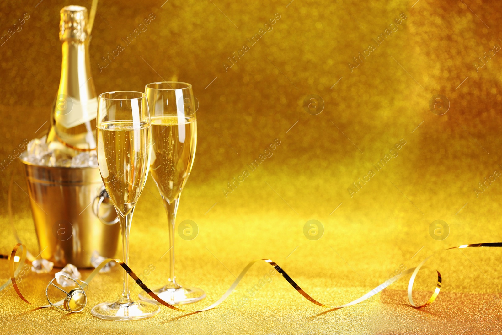 Photo of Champagne in glasses and ice bucket with bottle on golden background. Space for text