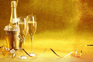 Photo of Champagne in glasses and ice bucket with bottle on golden background. Space for text