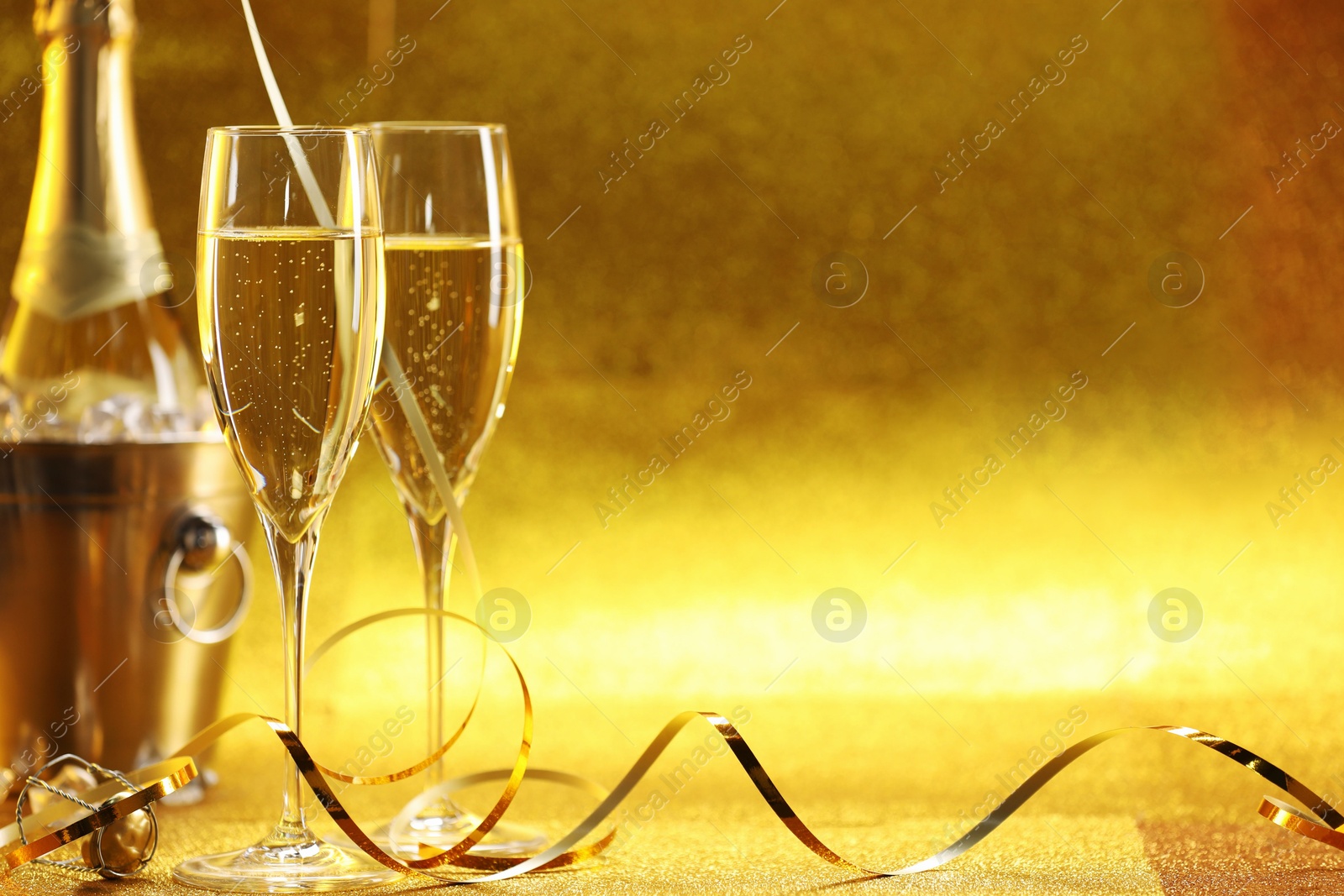 Photo of Champagne in glasses and ice bucket with bottle on golden background. Space for text