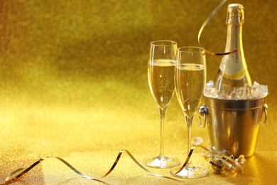 Photo of Champagne in glasses and ice bucket with bottle on golden background. Space for text