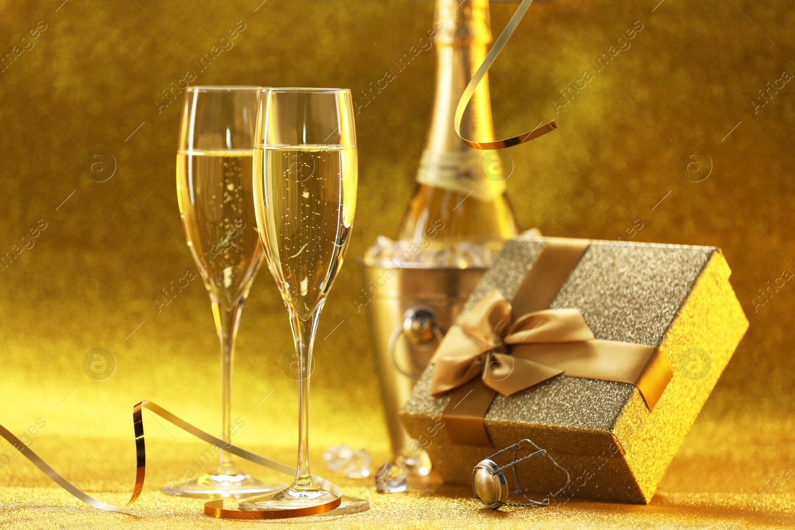 Photo of Champagne, gift box and streamers on golden background