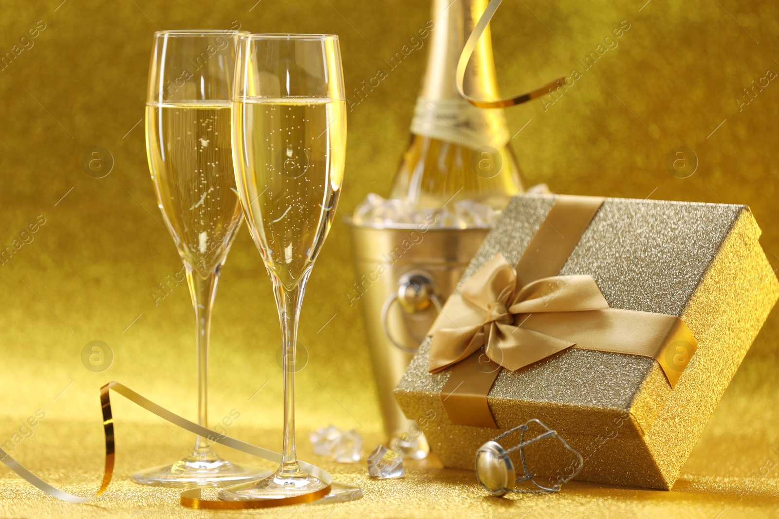 Photo of Champagne, gift box and streamers on golden background, closeup