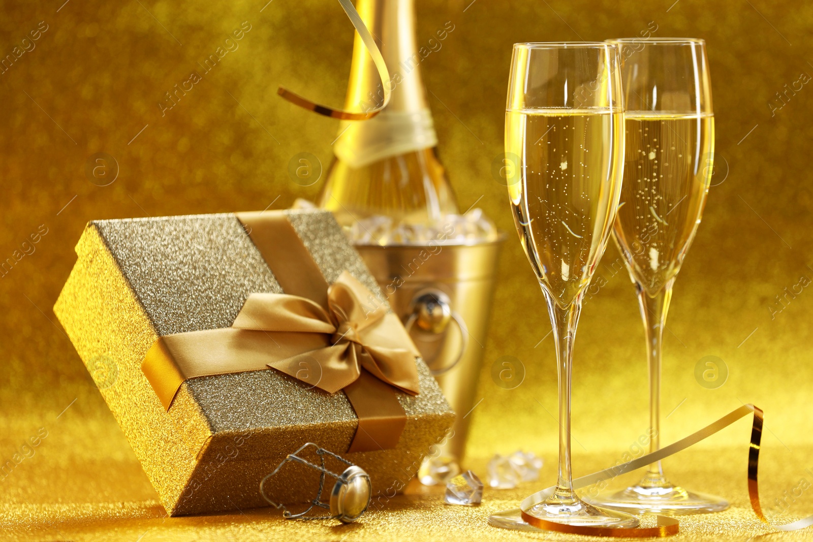 Photo of Champagne, gift box and streamers on golden background, closeup