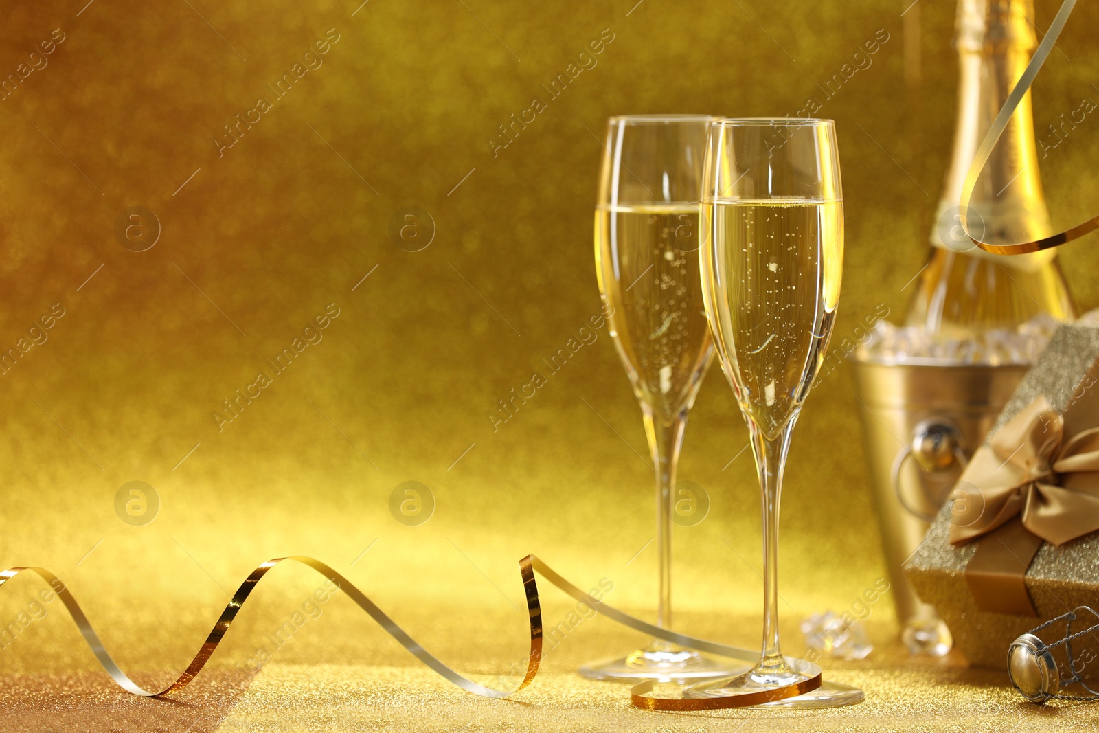 Photo of Champagne, gift box and streamers on golden background. Space for text