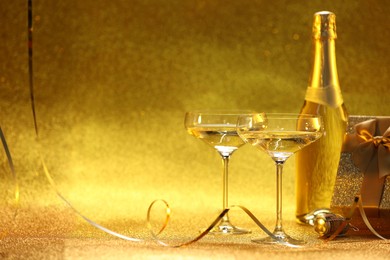 Photo of Champagne, gift box and streamers on golden background. Space for text