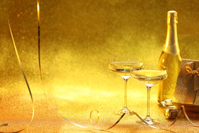 Photo of Champagne, gift box and streamers on golden background. Space for text