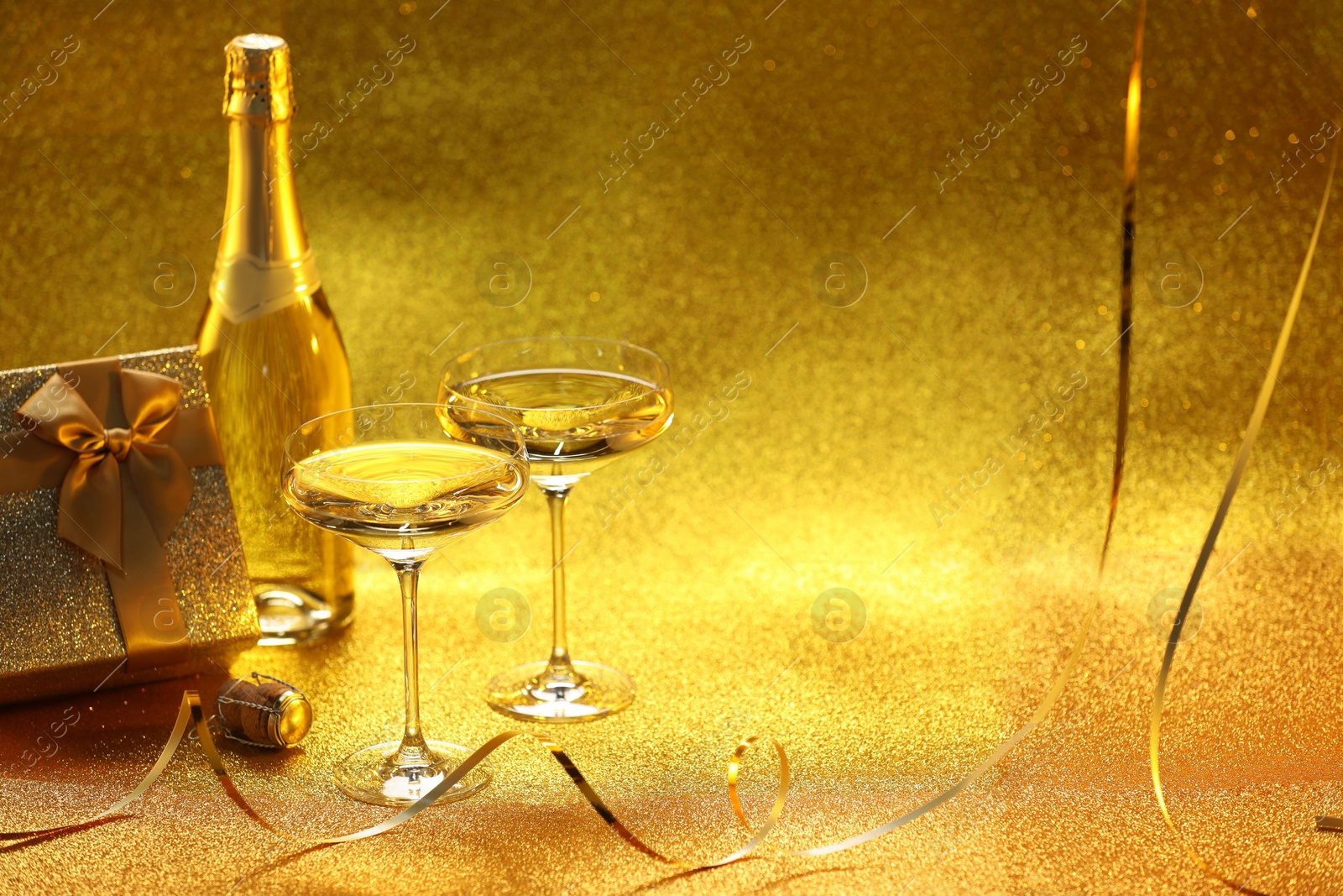 Photo of Champagne, gift box and streamers on golden background. Space for text