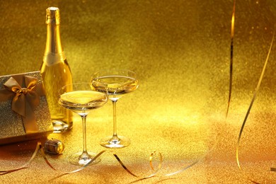 Photo of Champagne, gift box and streamers on golden background. Space for text