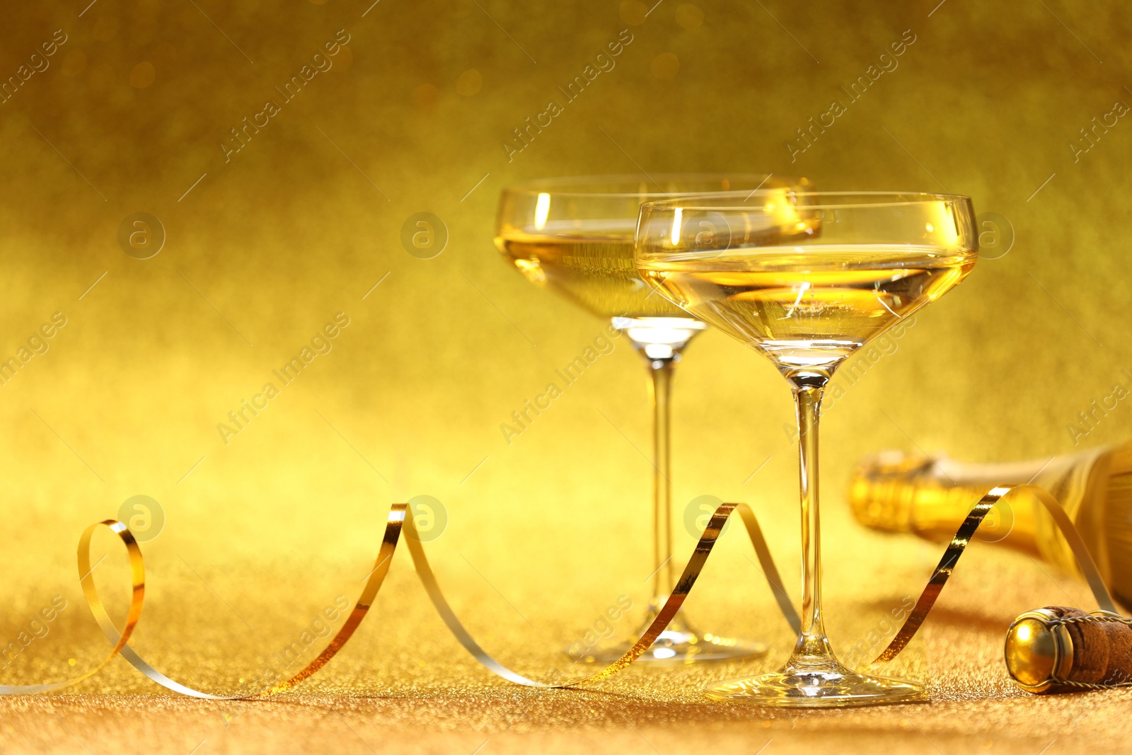 Photo of Champagne in glasses and bottle on golden background. Space for text