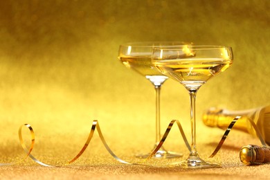 Photo of Champagne in glasses and bottle on golden background. Space for text