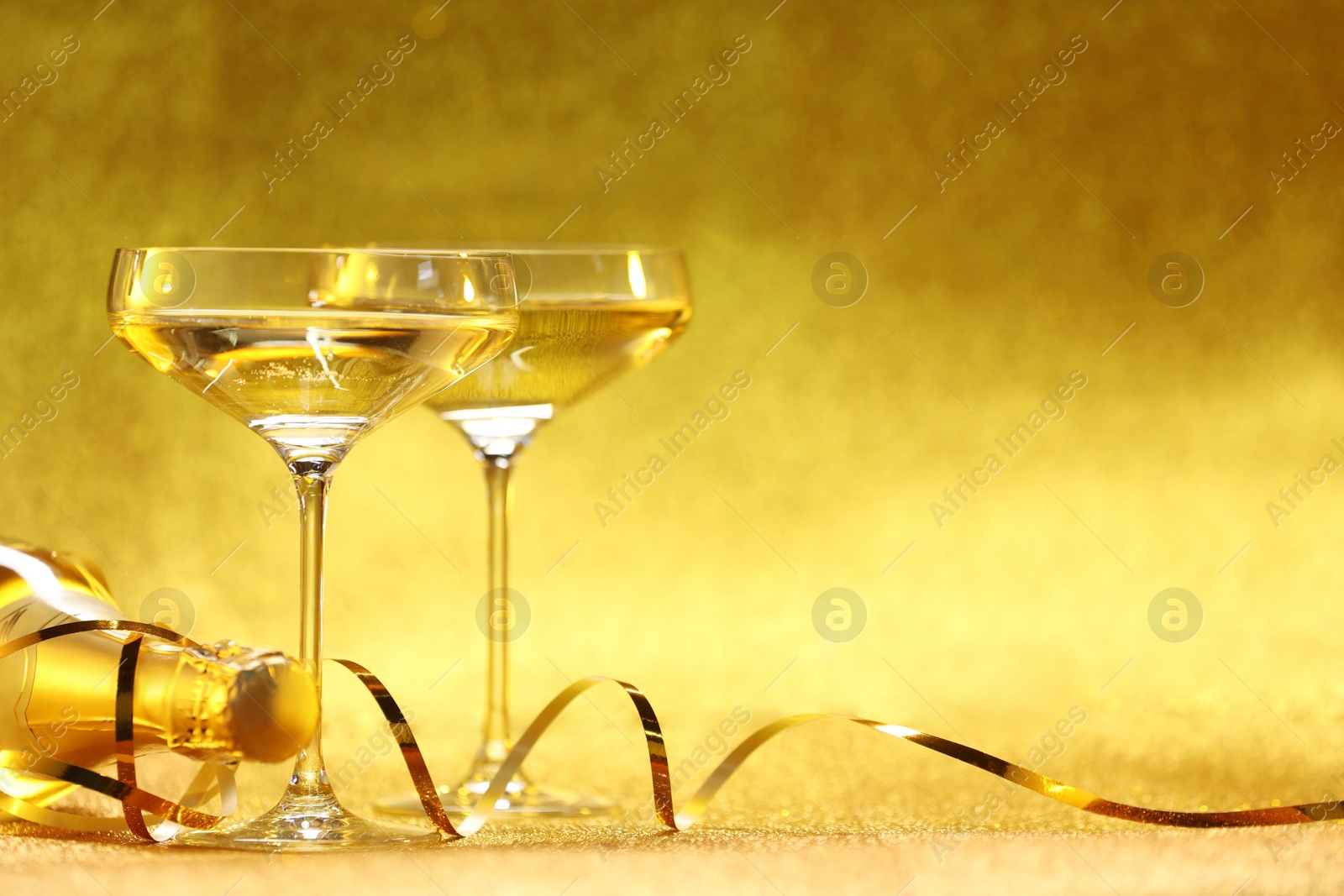 Photo of Champagne in glasses and bottle on golden background. Space for text