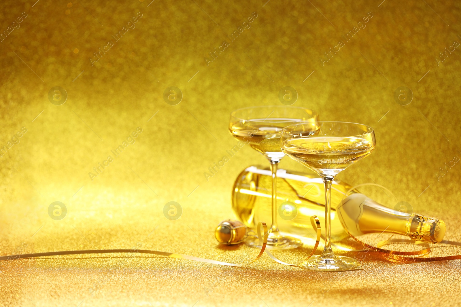 Photo of Champagne in glasses and bottle on golden background. Space for text