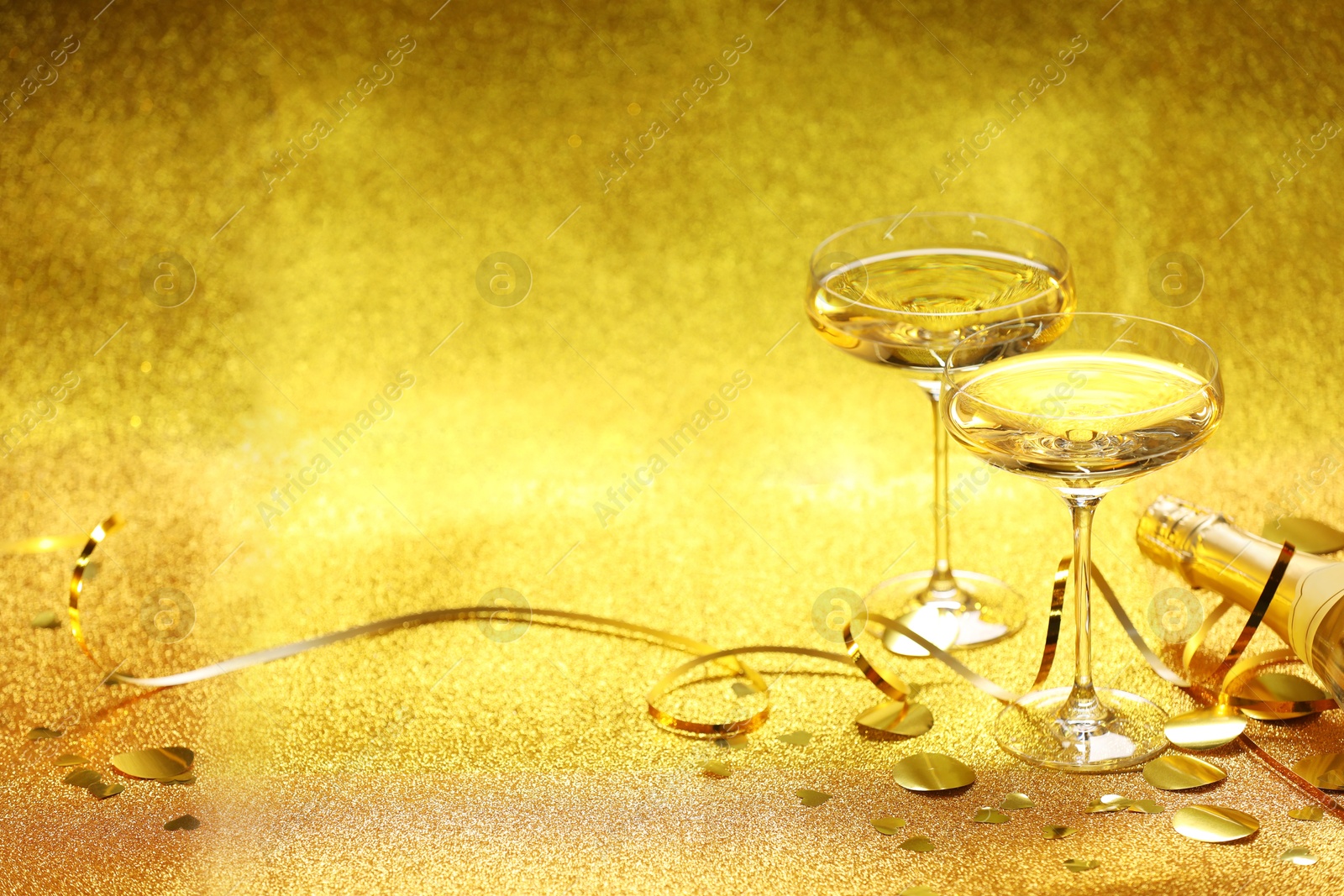 Photo of Champagne, confetti and streamers on golden background. Space for text