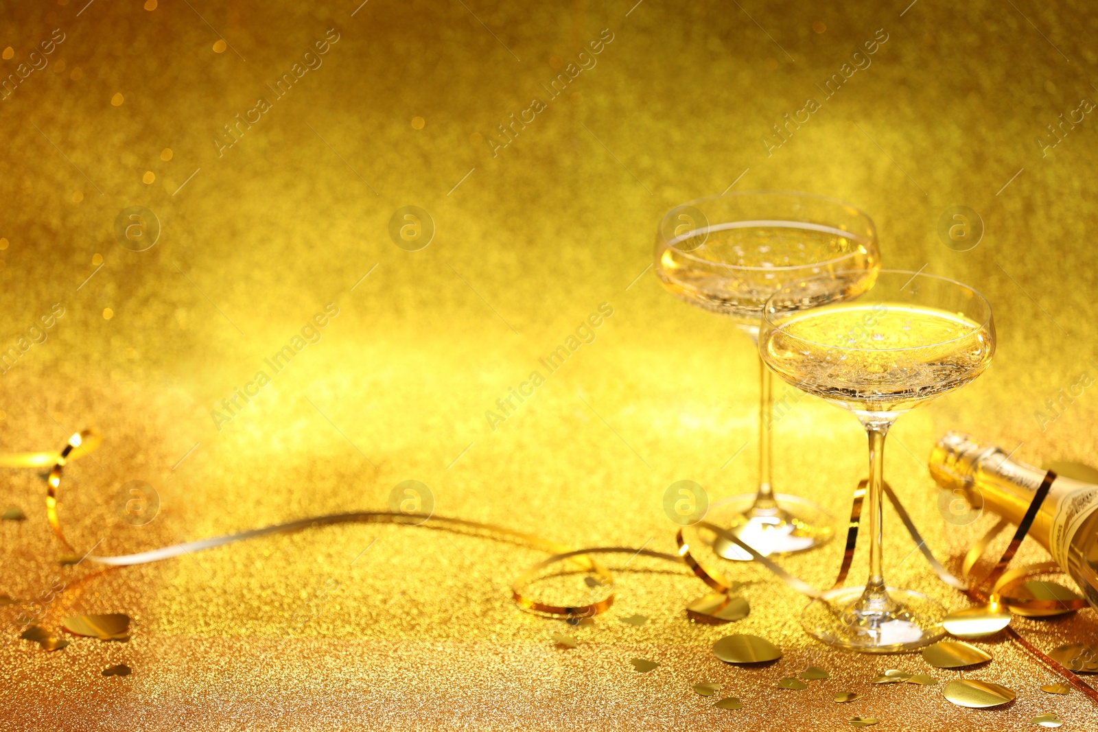 Photo of Champagne, confetti and streamers on golden background. Space for text