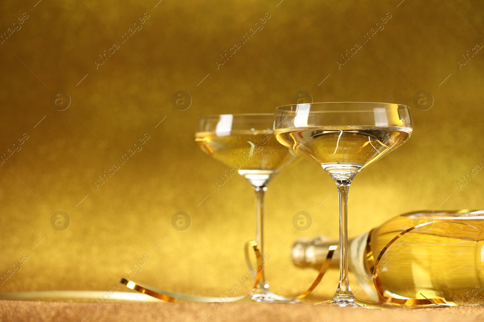 Photo of Champagne in glasses and bottle on golden background. Space for text