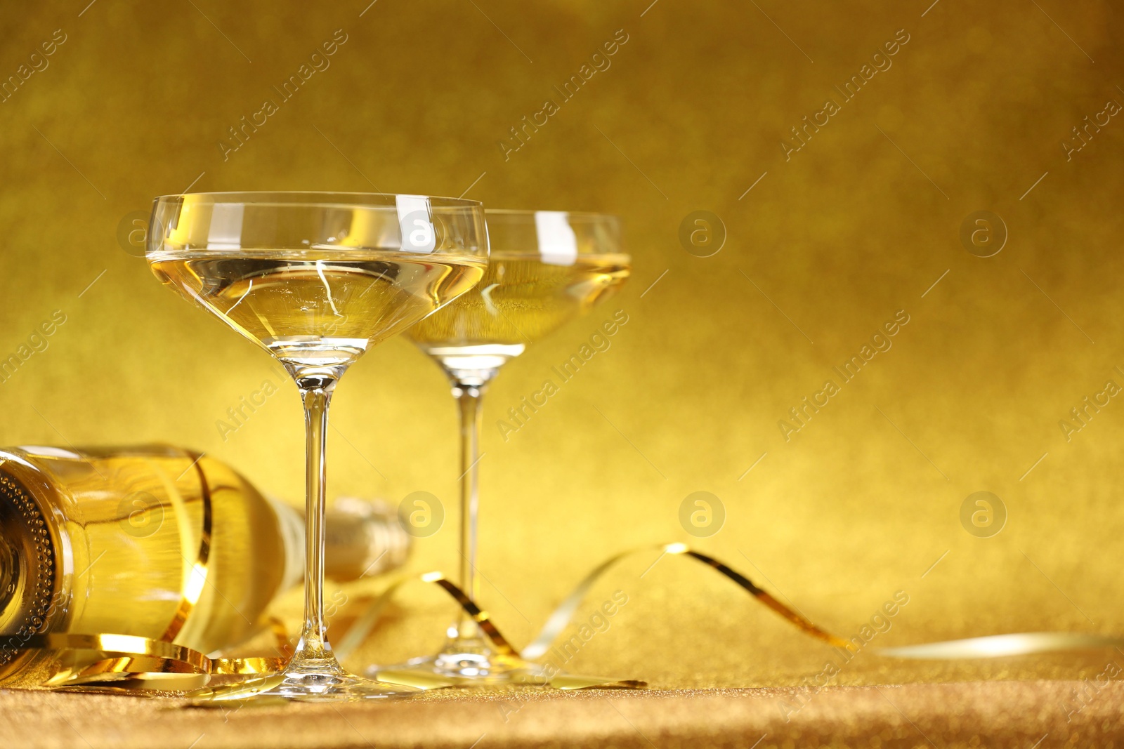 Photo of Champagne, confetti and streamers on golden background. Space for text