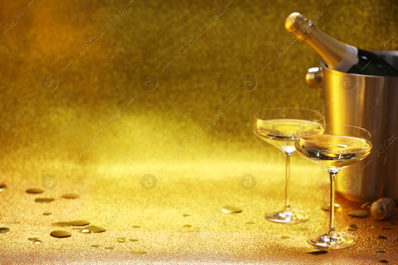 Photo of Champagne in glasses and ice bucket with bottle on golden background. Space for text