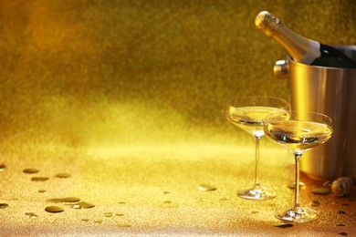 Photo of Champagne in glasses and ice bucket with bottle on golden background. Space for text