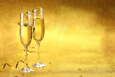 Photo of Champagne in glasses, confetti and streamers on golden background. Space for text