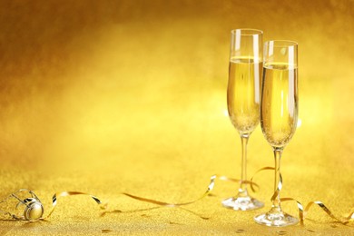 Photo of Champagne in glasses, confetti and streamers on golden background. Space for text