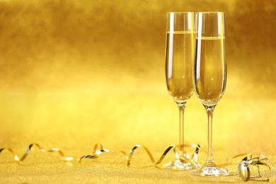 Photo of Champagne in glasses and streamers on golden background. Space for text