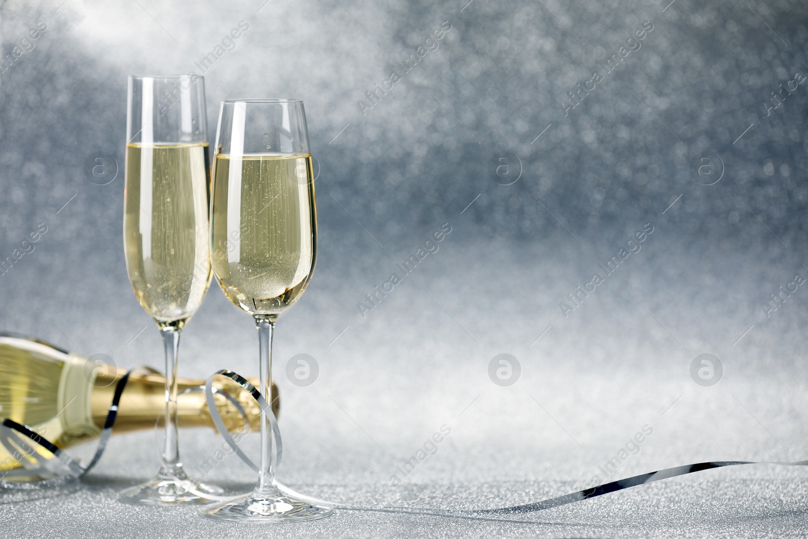 Photo of Champagne in glasses and bottle on silver background. Space for text