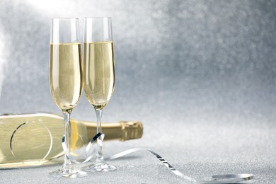 Photo of Champagne in glasses and bottle on silver background. Space for text