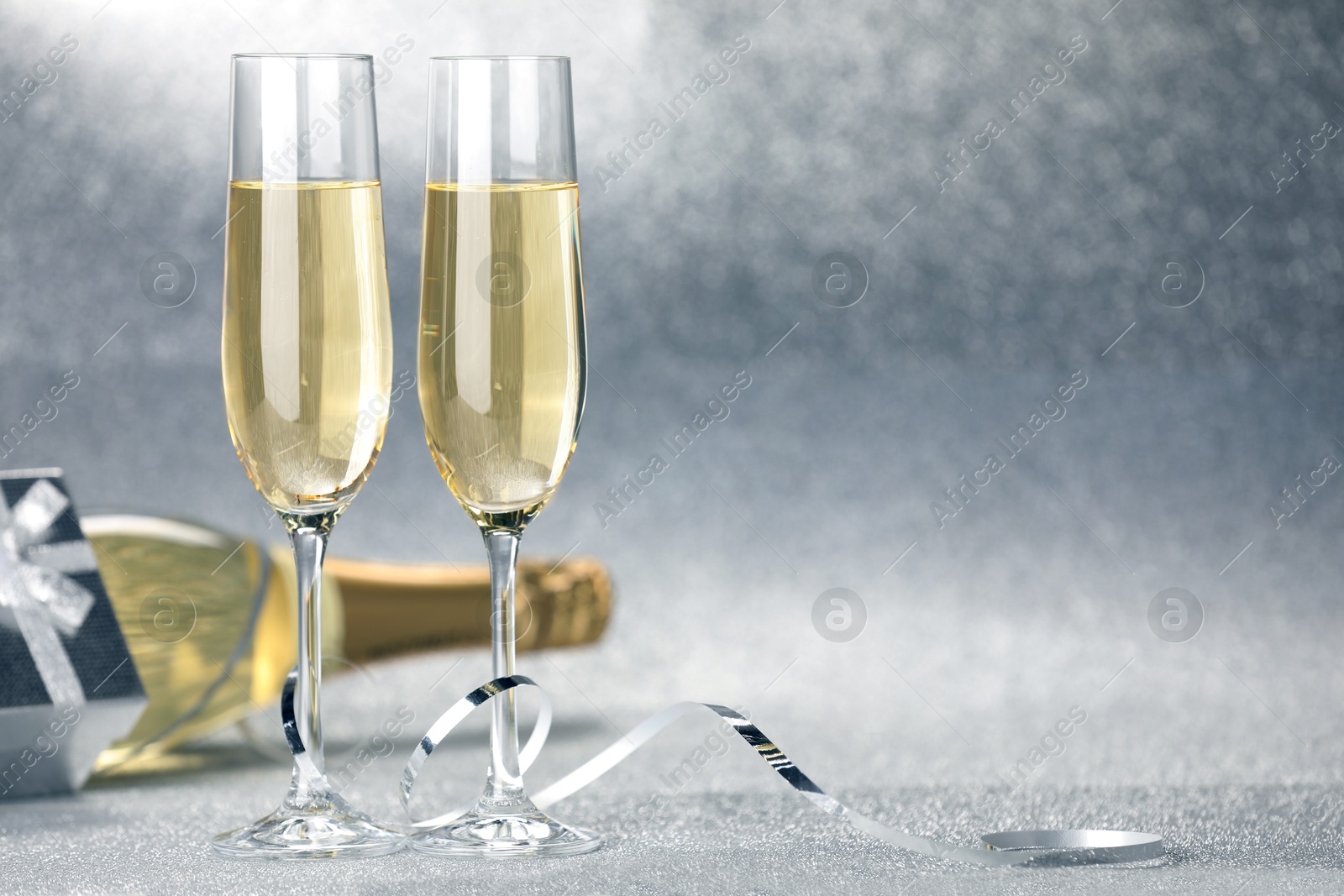 Photo of Champagne in glasses, bottle, gift box and streamers on silver background. Space for text