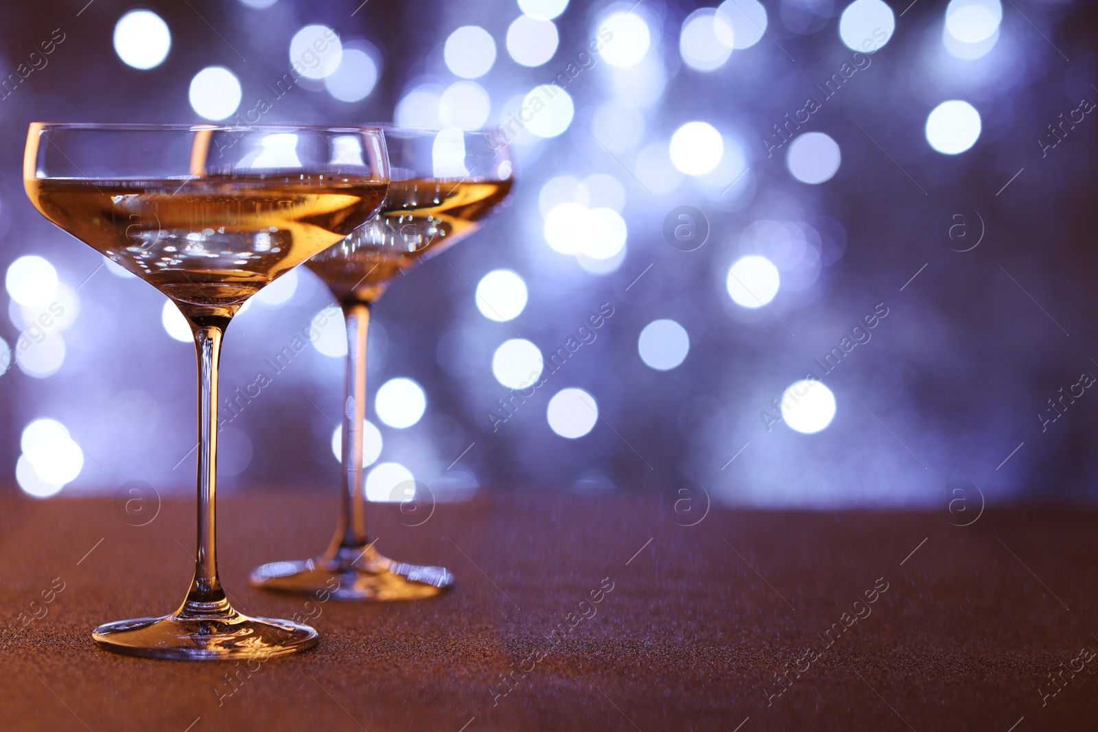 Photo of Champagne in glasses on table against blurred lights. Space for text