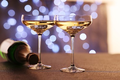 Photo of Champagne in glasses and bottle on table against blurred lights, closeup