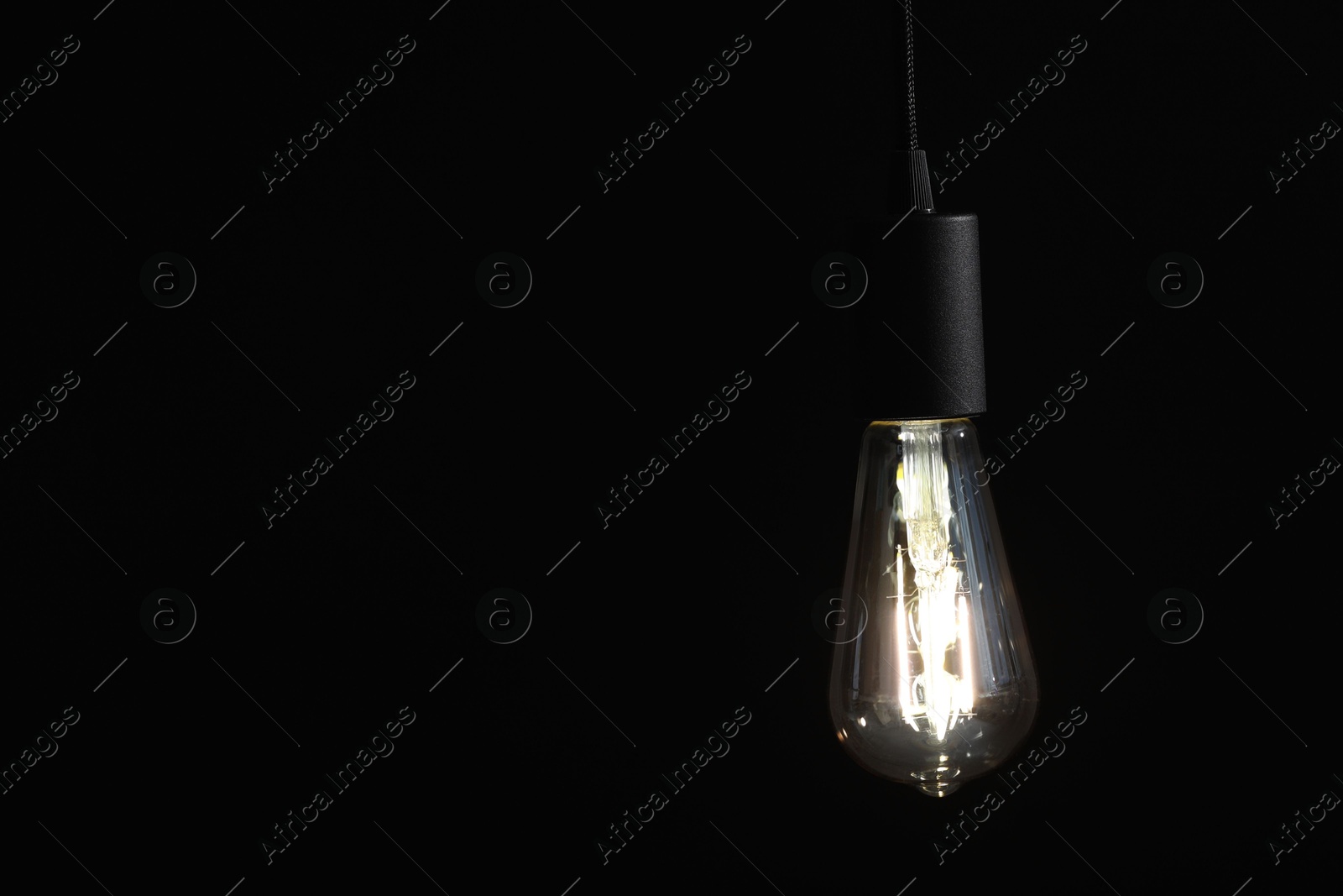 Photo of Glowing light bulb hanging on dark background. Space for text