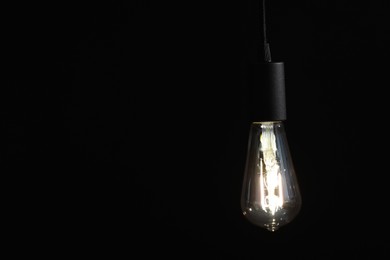 Photo of Glowing light bulb hanging on dark background. Space for text