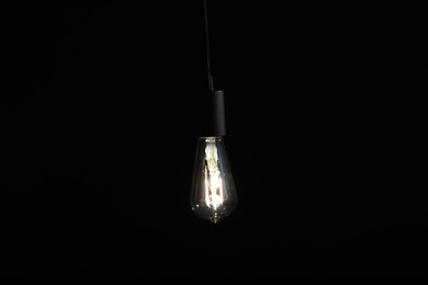 Photo of Glowing light bulb hanging on dark background