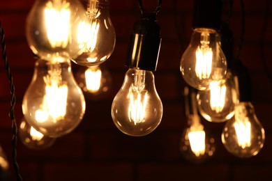 Photo of Glowing light bulbs hanging on dark background, closeup