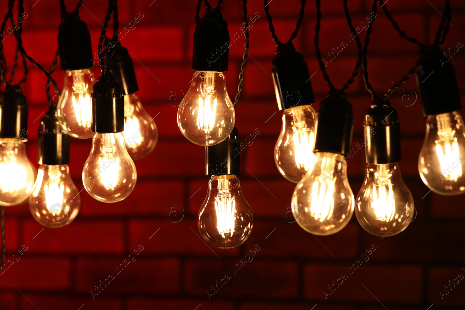 Photo of Glowing light bulbs hanging against brick wall, closeup