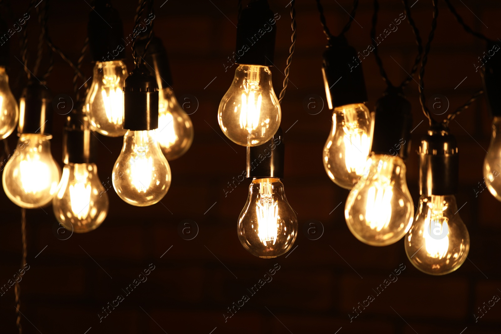 Photo of Glowing light bulbs hanging on dark background, closeup