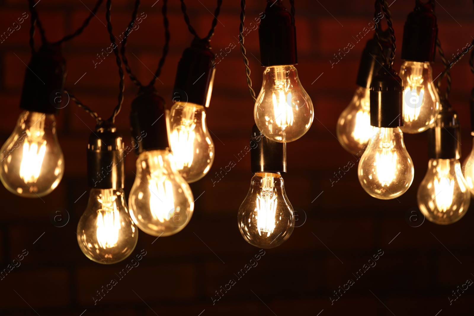 Photo of Glowing light bulbs hanging on dark background, closeup