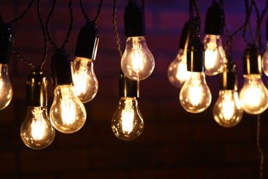 Photo of Glowing light bulbs hanging on dark background, closeup