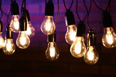 Photo of Glowing light bulbs hanging on dark background, closeup