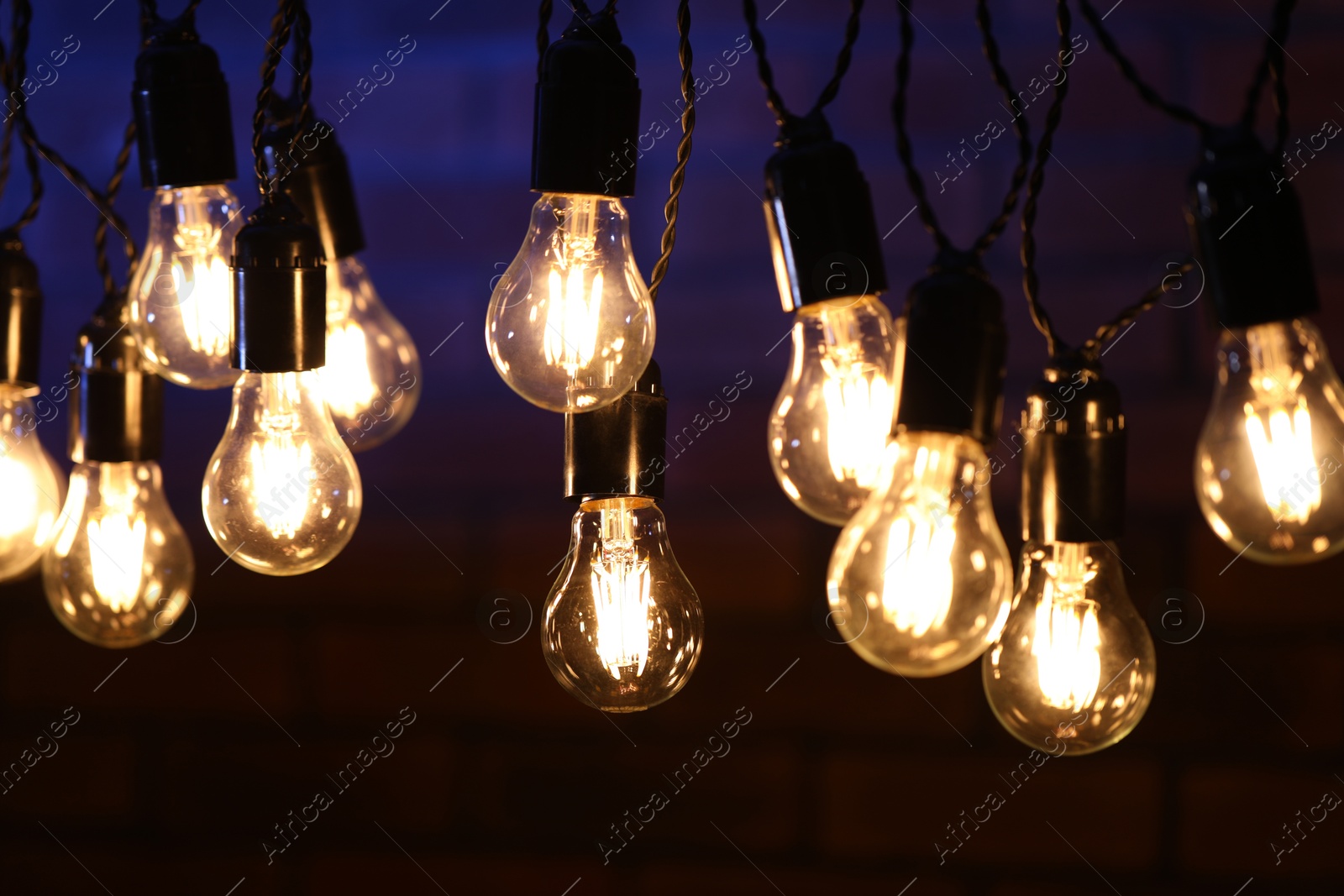 Photo of Glowing light bulbs hanging on dark background, closeup