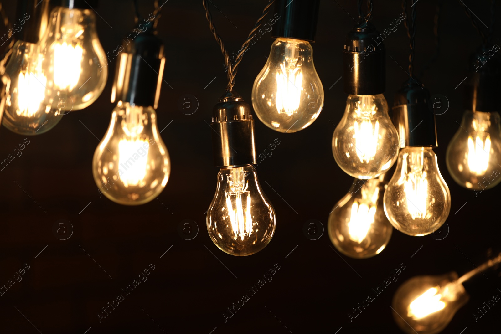 Photo of Glowing light bulbs hanging on dark background, closeup